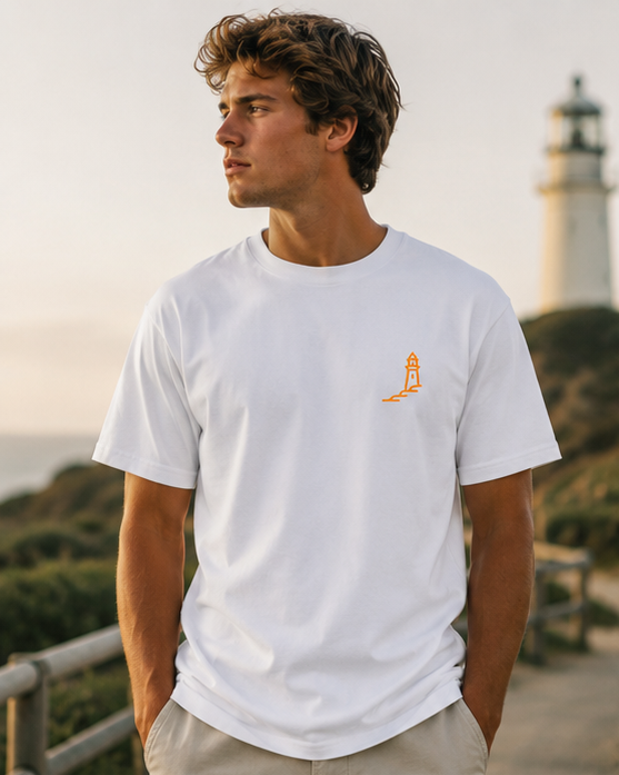 Modelo con camiseta blanca Amanecer Atlántico de Nómadas 24/7 junto a un faro