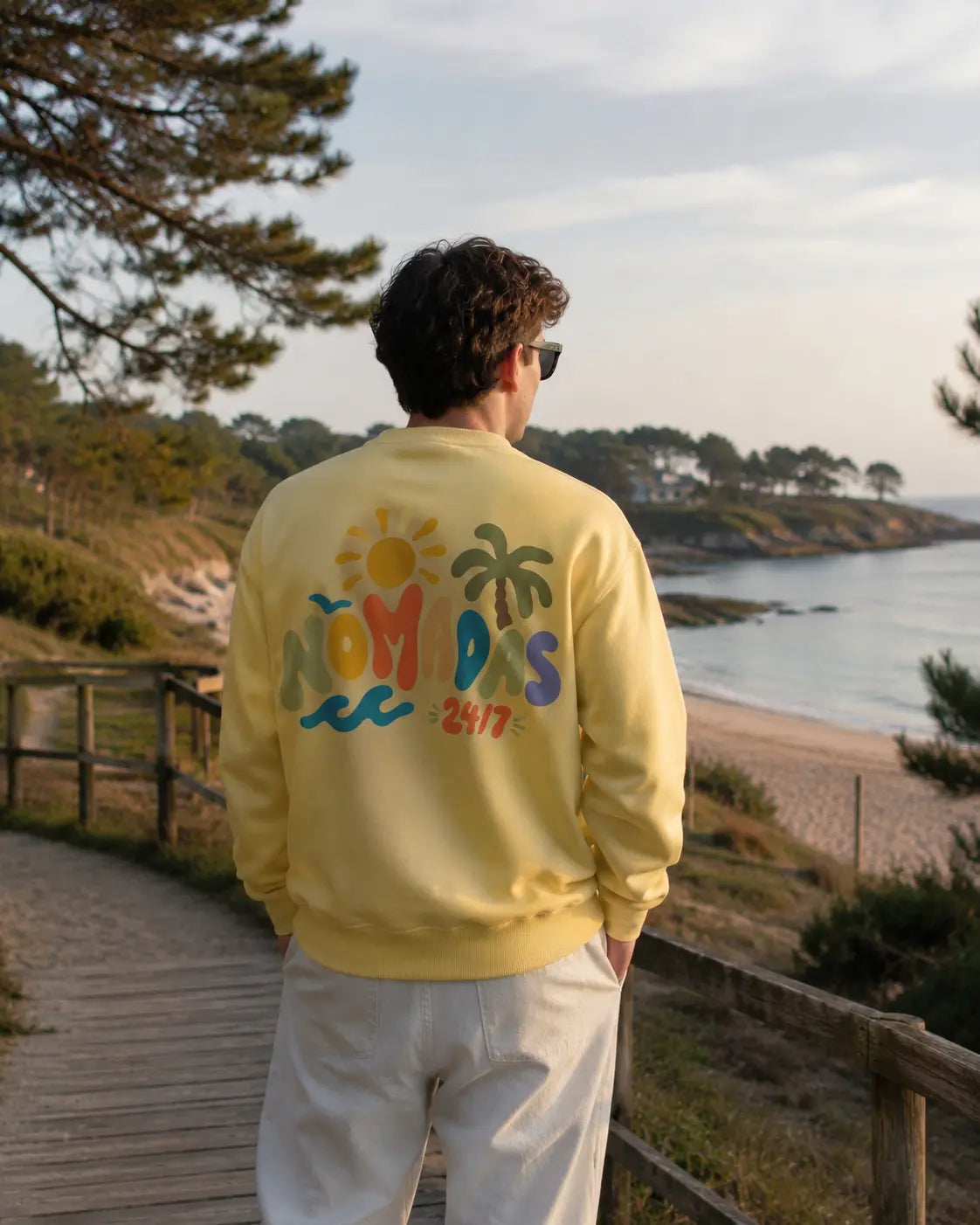 Modelo de espaldas con sudadera amarilla Verano 24/7 junto al mar