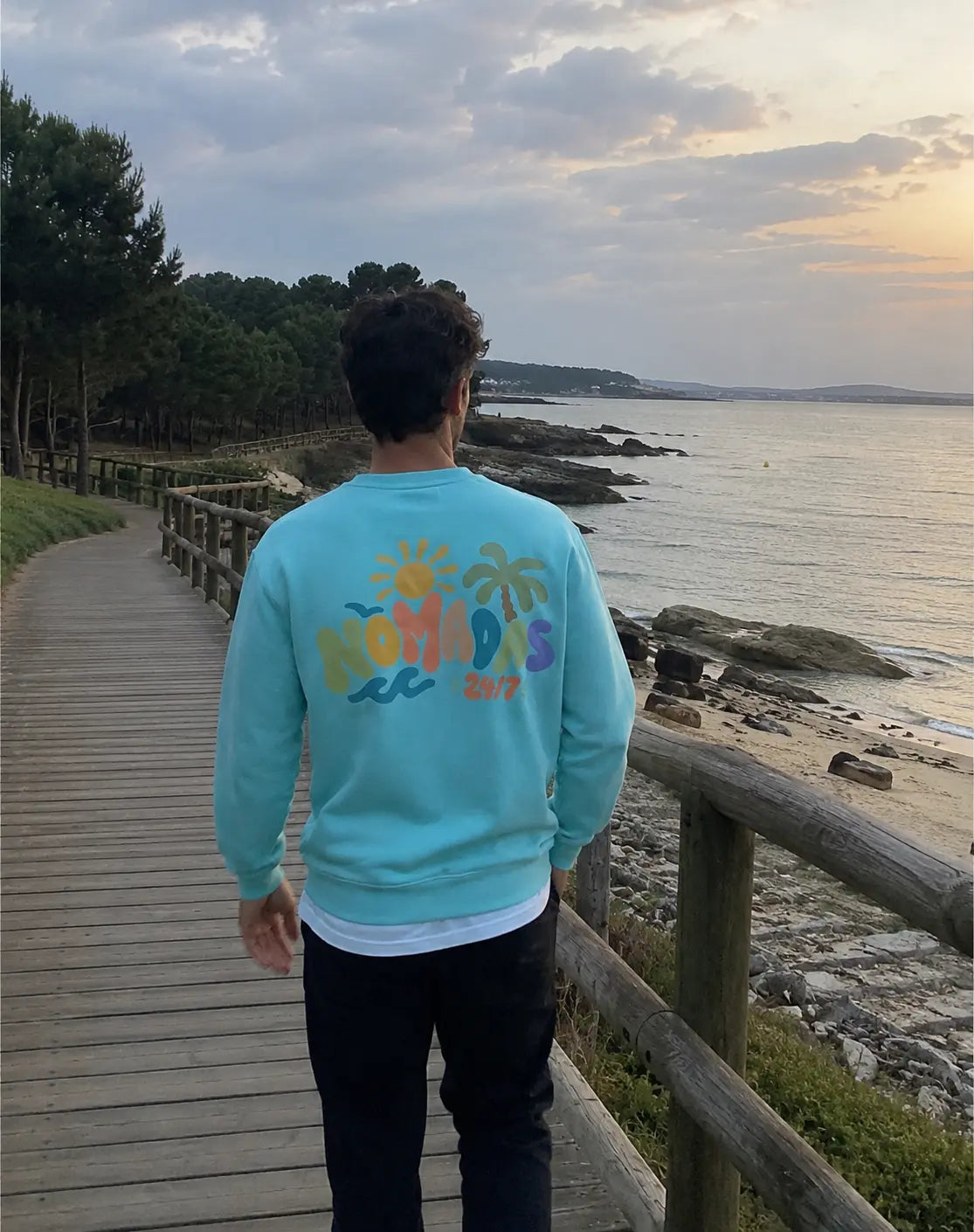 Modelo de espaldas con sudadera azul Verano 24/7 en la costa
